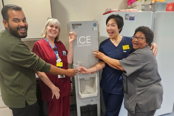 Members of staff standing in front of an ice machine holding cups of ice cubes.
