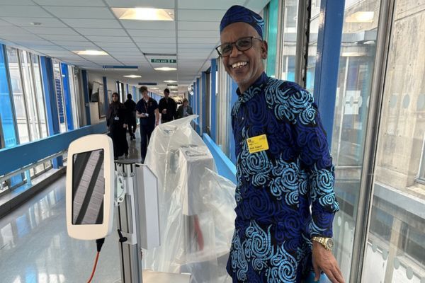 Abdi standing in a corridor next to a trolley with an iPad on it.