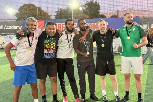 A group of staff in football clothes wearing winning medals and holding a trophy.